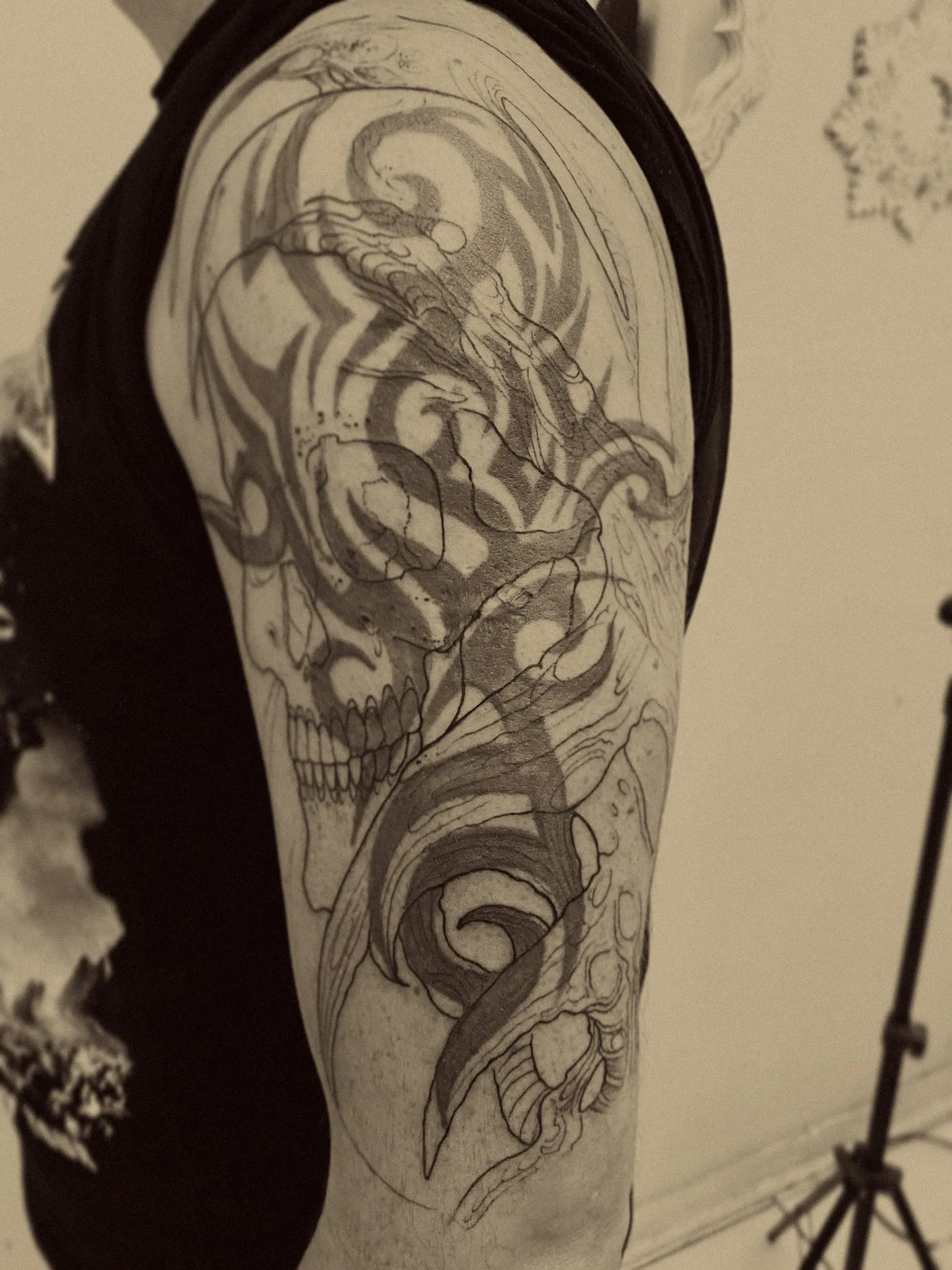 Calavera en negro y gris integrada a un tribal antiguo en el brazo