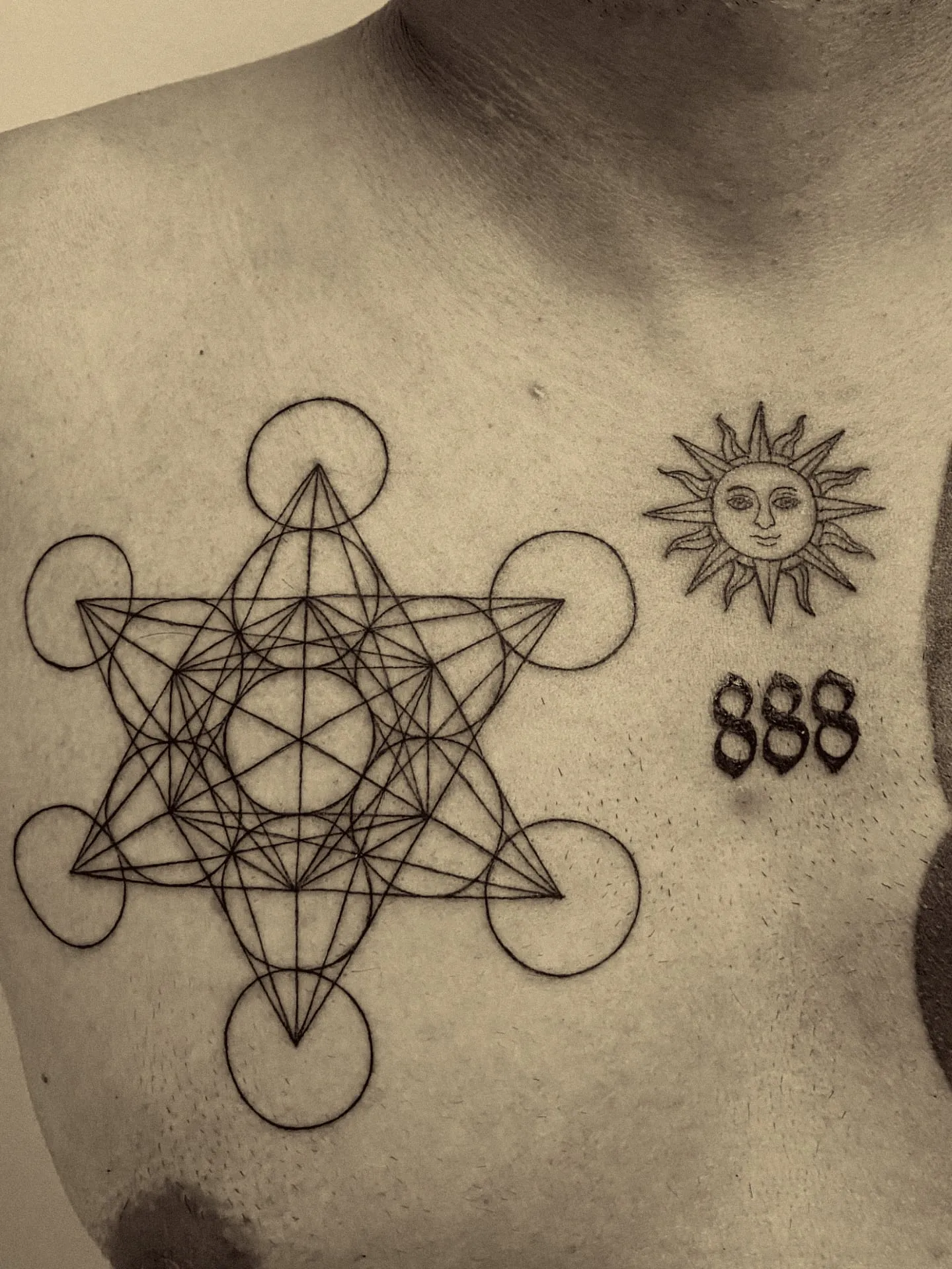 Cubo de Metatrón, un sol con rostro y el número 888 en línea fina sobre el pecho