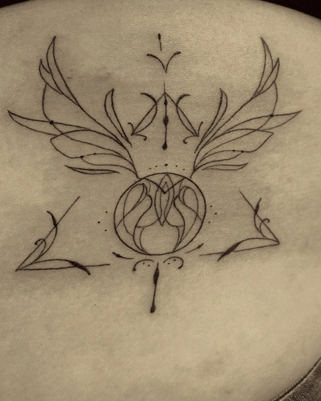 Sigilo ornamental con alas y un triángulo en línea fina en la espalda alta