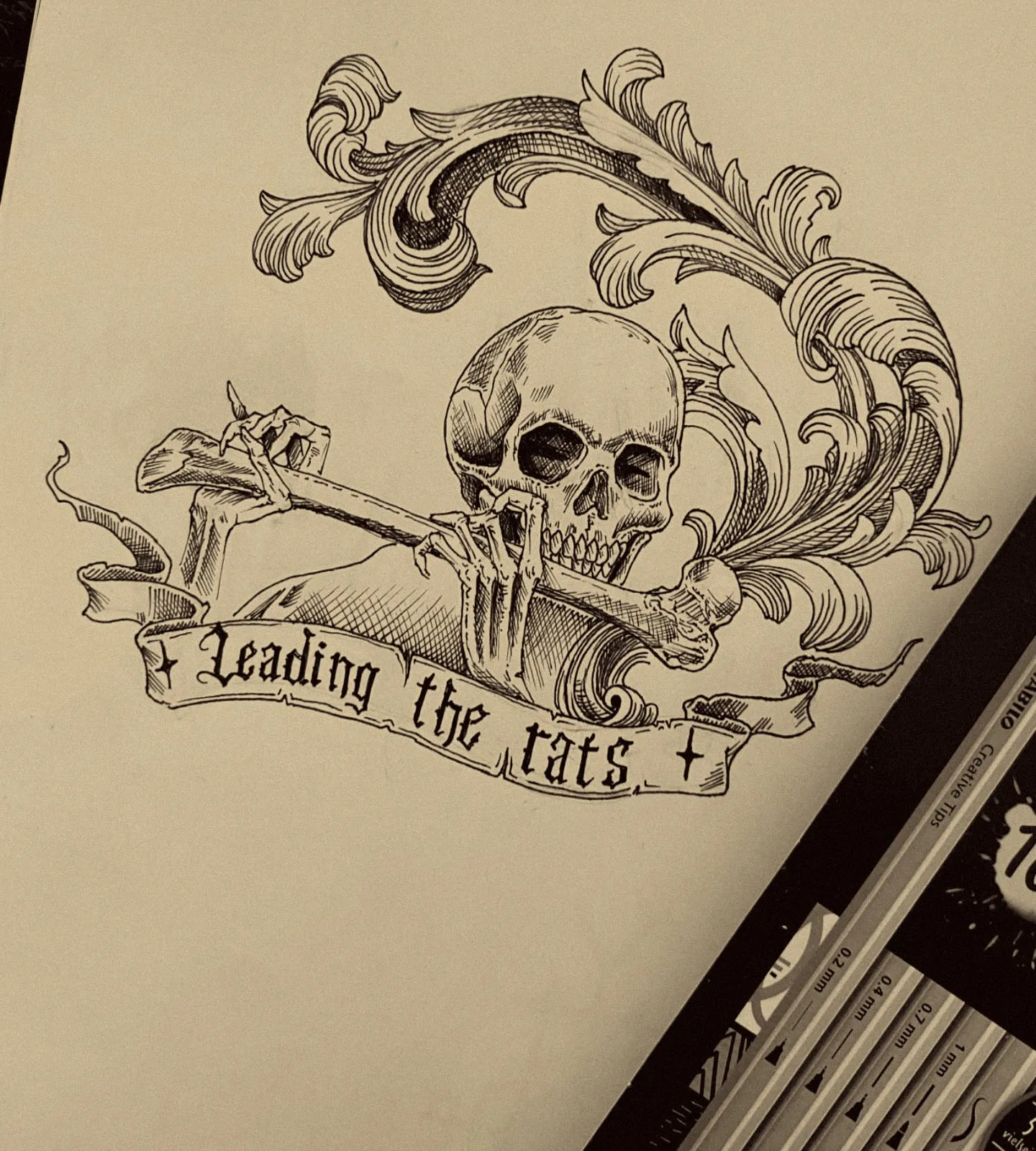 Dibujo a tinta de una calavera que muerde un hueso entre volutas, con la cinta Leading the rats
