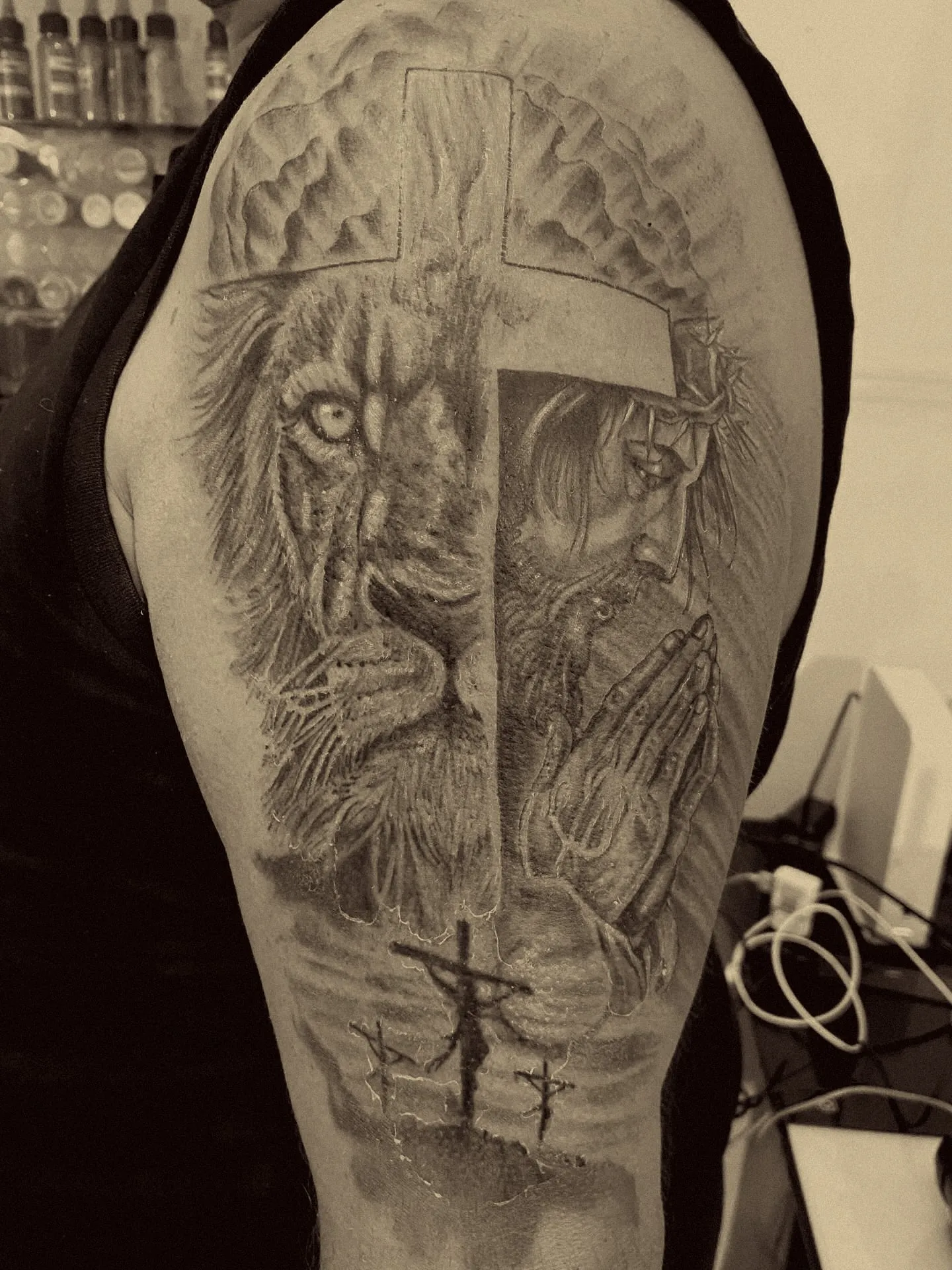 León y Cristo en oración divididos por una cruz, con el Calvario abajo, en realismo negro y gris en el brazo